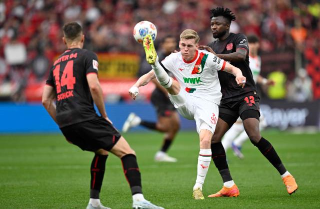 Bayer Leverkusen's Czech forward #14 Patrik Schick (L), Bayer Leverkusen's Burkinabe defender #12 Edmond Tapsoba (R) and Augsburg's German midfielder #30 Anton Kade (C) vie for the ball during the German first division Bundesliga football match between Bayer 04 Leverkusen and FC Augsburg in Leverkusen, western Germany, on April 18, 2026. (Photo by INA FASSBENDER / AFP) / DFL REGULATIONS PROHIBIT ANY USE OF PHOTOGRAPHS AS IMAGE SEQUENCES AND/OR QUASI-VIDEO