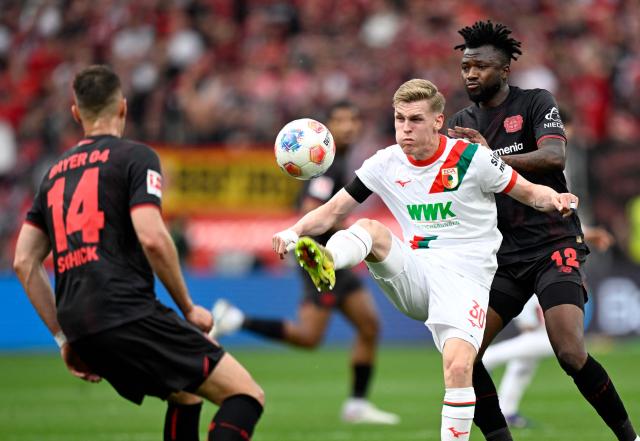 Bayer Leverkusen's Czech forward #14 Patrik Schick (L), Bayer Leverkusen's Burkinabe defender #12 Edmond Tapsoba (R) and Augsburg's German midfielder #30 Anton Kade (C) vie for the ball during the German first division Bundesliga football match between Bayer 04 Leverkusen and FC Augsburg in Leverkusen, western Germany, on April 18, 2026. (Photo by INA FASSBENDER / AFP) / DFL REGULATIONS PROHIBIT ANY USE OF PHOTOGRAPHS AS IMAGE SEQUENCES AND/OR QUASI-VIDEO