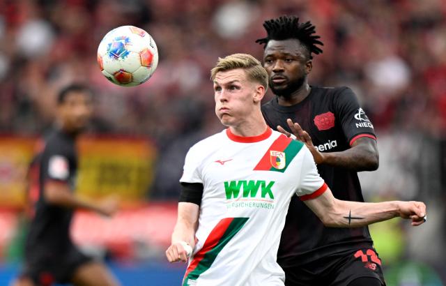 Bayer Leverkusen's Burkinabe defender #12 Edmond Tapsoba (R) and Augsburg's German midfielder #30 Anton Kade vie for the ball during the German first division Bundesliga football match between Bayer 04 Leverkusen and FC Augsburg in Leverkusen, western Germany, on April 18, 2026. (Photo by INA FASSBENDER / AFP) / DFL REGULATIONS PROHIBIT ANY USE OF PHOTOGRAPHS AS IMAGE SEQUENCES AND/OR QUASI-VIDEO
