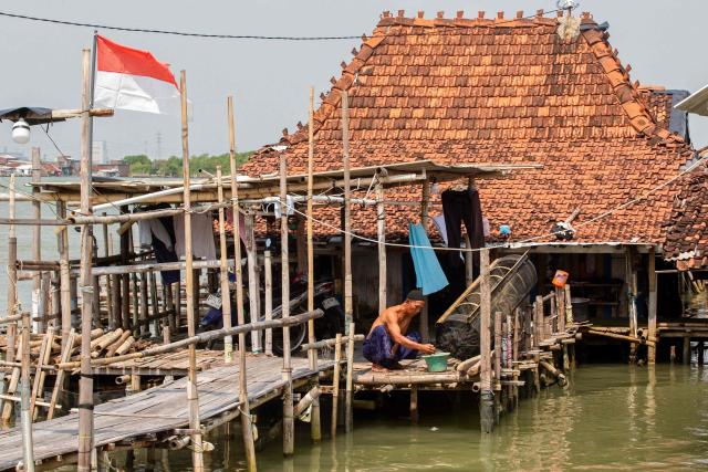 A man works outside a house partially submerged in seawater due to tidal flooding at the Timbulsloko village in Demak, Central Java on April 18, 2026. (Photo by DEVI RAHMAN / AFP)