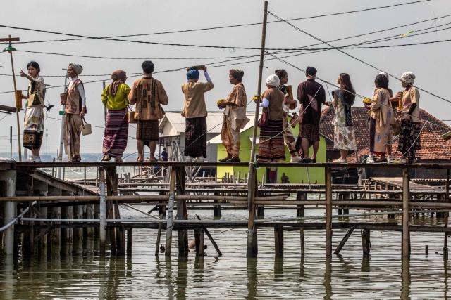 Local models wearing traditional outfits wait to cross a bridge that connects houses partially submerged in seawater due to tidal flooding at the Timbulsloko village in Demak, Central Java on April 18, 2026. (Photo by DEVI RAHMAN / AFP)