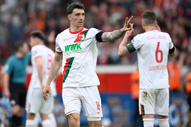 Augsburg's Swiss defender #16 Cedric Zesiger (C) celebrates with Augsburg's Dutch defender #06 Jeffrey Gouweleeuw (R) at the end of the German first division Bundesliga football match between Bayer 04 Leverkusen and FC Augsburg in Leverkusen, western Germany, on April 18, 2026. (Photo by INA FASSBENDER / AFP) / DFL REGULATIONS PROHIBIT ANY USE OF PHOTOGRAPHS AS IMAGE SEQUENCES AND/OR QUASI-VIDEO