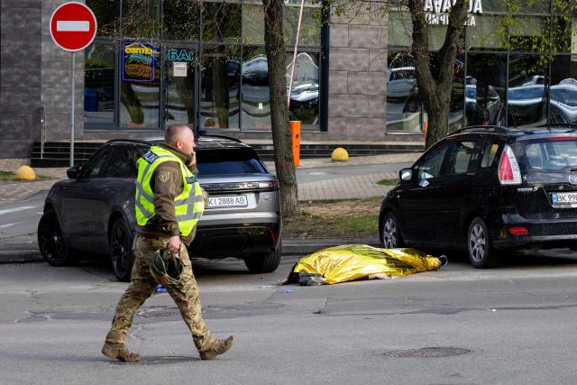 EDITORS NOTE: Graphic content / A policeman walks past a body of a person shot by a gunman outside a supermarket in Kyiv on April 18, 2026. A gunman opened fire in Kyiv on April 18, 2026, killing at least five people, wounding others and taking hostages at a supermarket before being killed during an arrest attempt, officials said. Ukrainian President said that at least five people were dead and 10 hospitalised with wounds and trauma after the shooting in a residential district of the capital. (Photo by Serhii Okunev / AFP)