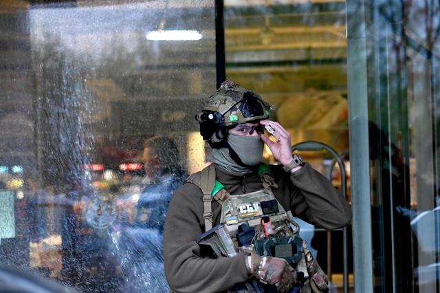 A special team policeman stands in front of a hole made from a bullet in the window of a supermarket after a shooting in Kyiv on April 18, 2026. A gunman opened fire in Kyiv on April 18, 2026, killing at least five people, wounding others and taking hostages at a supermarket before being killed during an arrest attempt, officials said. Ukrainian President said that at least five people were dead and 10 hospitalised with wounds and trauma after the shooting in a residential district of the capital. (Photo by Sergei SUPINSKY / AFP)