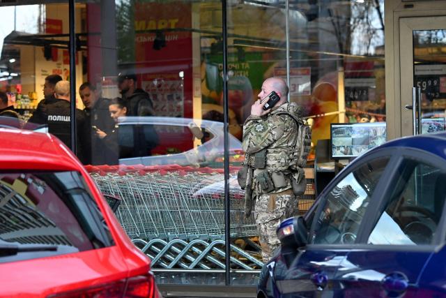 A special team policeman talks on a phone in front of a supermarket after a shooting in Kyiv on April 18, 2026. A gunman opened fire in Kyiv on April 18, 2026, killing at least five people, wounding others and taking hostages at a supermarket before being killed during an arrest attempt, officials said. Ukrainian President said that at least five people were dead and 10 hospitalised with wounds and trauma after the shooting in a residential district of the capital. (Photo by Sergei SUPINSKY / AFP)