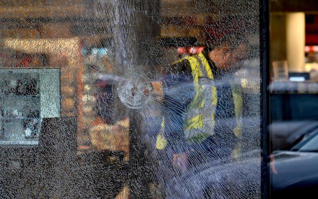A policeman walks past a hole made from a bullet in a window of a supermarket after a shooting in Kyiv on April 18, 2026. A gunman opened fire in Kyiv on April 18, 2026, killing at least five people, wounding others and taking hostages at a supermarket before being killed during an arrest attempt, officials said. Ukrainian President said that at least five people were dead and 10 hospitalised with wounds and trauma after the shooting in a residential district of the capital. (Photo by Sergei SUPINSKY / AFP)