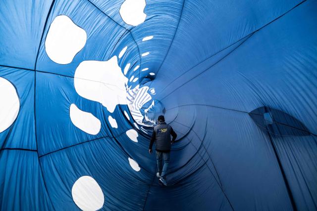 A participant walks through a kite depicting a whale while taking part in the 39th International Kite Festival (RICV) at the beach of Berck-sur-Mer, northern France, on April 18, 2026. Some 450 kite flyers from 28 countries attended the 39th Berck-sur-Mer International Kite Festival. The event is one of the largest of its kind and offers “a touch of magic” to counter the “gloom of everyday life”. (Photo by Sameer Al-DOUMY / AFP)