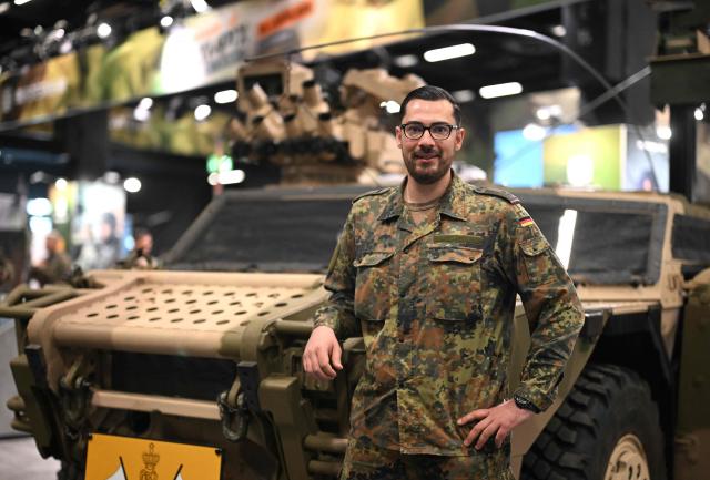 Lieutenant Colonel Peter stands at a reconnaissance vehicle of the Bundeswehr at their booth at the FIBO trade show for health, fitness and wellness in Cologne, western Germany on April 16, 2026. “We’re looking for people who are young, sporty, dynamic and motivated. And here we’ve got them right on the spot,” explains Peter, a 30-year-old lieutenant in charge of the stand, in an interview with AFP. (Photo by Ina FASSBENDER / AFP)