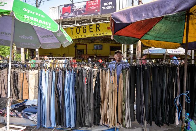 A vendor arranges trousers as he waits for customers at his clothing stall along a street in Surabaya on April 19, 2026. (Photo by JUNI KRISWANTO / AFP)