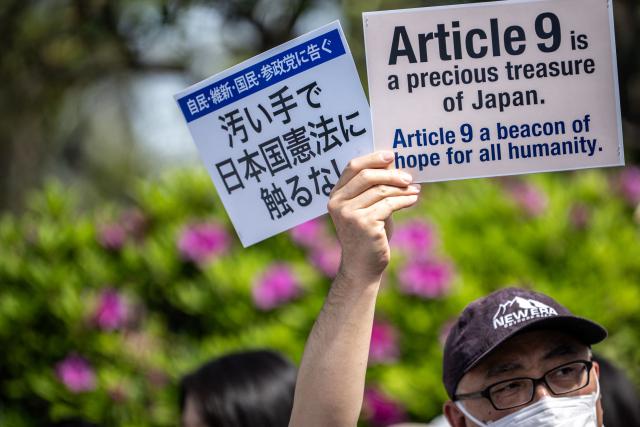 A man holds placards reading "Article 9 is a precious treasure of Japan. Article 9 a beacon of hope for all humanity." (R) and "To the LDP, Ishin, the Democratic Party for the People, and the Sanseito: Don’t lay a finger on the Constitution of Japan with your dirty hands" during the "No war! Don’t change the Constitution!" rally outside the main gate of the National Diet Building in Tokyo on April 19, 2026. Article 9 is a clause stipulating that the Japanese people have renounced war as a sovereign right of the nation and the threat or use of force as means of settling international disputes (Photo by Philip FONG / AFP)