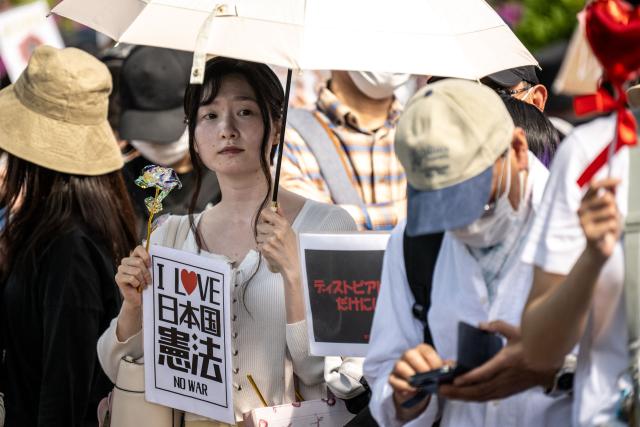 A woman holds a placard reading "I love the Constitution of Japan" during the "No war! Don’t change the Constitution!" rally outside the main gate of the National Diet Building, to call for the protection of Article 9 of the Constitution of Japan, in Tokyo on April 19, 2026. Article 9 is a clause stipulating that the Japanese people have renounced war as a sovereign right of the nation and the threat or use of force as means of settling international disputes (Photo by Philip FONG / AFP)