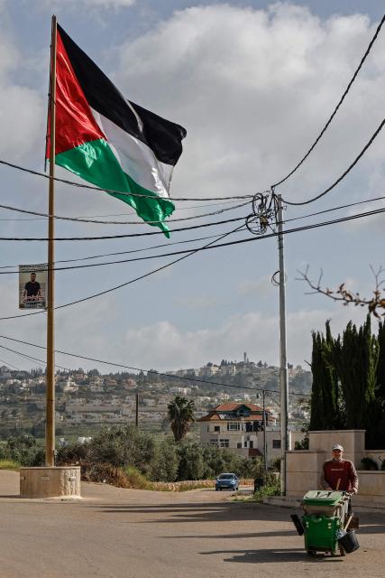 A worker walks past a Palestinian flag installed along a street in Turmus Ayya village, north of Ramallah in the Israeli-occupied West Bank on April 19, 2026. Violence in the West Bank, which Israel has occupied since 1967, has risen sharply since the October 7, 2023 Hamas attack on Israel triggered the Gaza war. There has also been a spike in deadly attacks by Israeli settlers in the West Bank since the start of the Iran war on February 28, Palestinian authorities and the United Nations have said. (Photo by Zain JAAFAR / AFP)