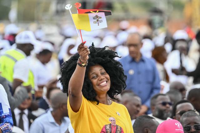 A faithful holding Vatican and Angola flags cheers as Pope Leo XIV (unssen) arrives in the Popemobile to lead a Holy Mass in Kalimba on the seventh day of an 11-day apostolic journey to Africa, on April 19, 2026. (Photo by Alberto PIZZOLI / AFP)