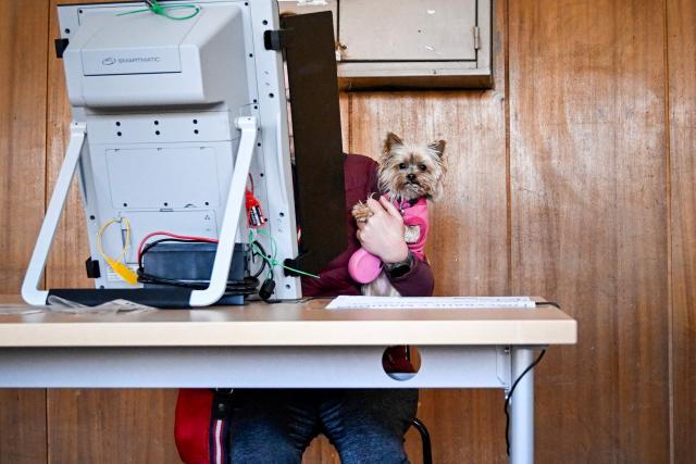 A voter casts her ballot accompanied by her dog using an Electronic Voting Machine (EVM) at the polling station during Bulgaria's parliamentary elections in Sofia on April 19, 2026. Bulgarians vote in the country's eighth election in five years today, with ex-president Rumen Radev's grouping tipped to win on a pledge to fight corruption, after an anti-graft movement triggered a long political crisis. (Photo by Dimitar KYOSEMARLIEV / AFP)