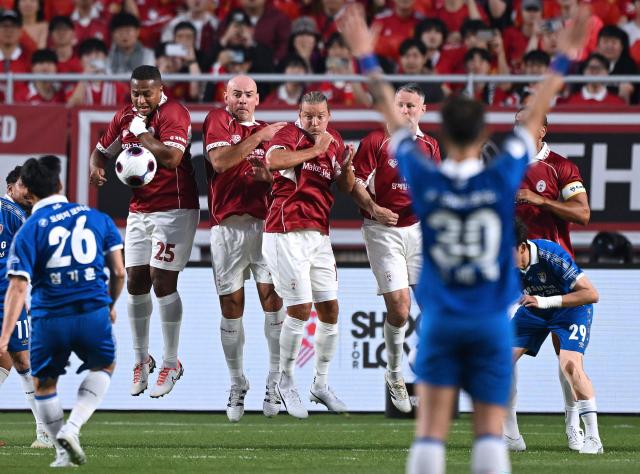 OGFC's players (red) try to block a free kick by Suwon Samsung Legends' Yeom Ki-hun (L) during a friendly football match between OGFC, a newly formed football club by Premier League legends from Manchester United, and South Korea's Suwon Samsung Legends in Suwon on April 19, 2026. (Photo by Jung Yeon-je / AFP)