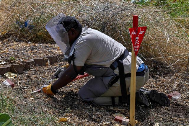 TOPSHOT - A member of the Dutch Migration Council (DRC), and Jasmar Human Security Organization uses a metal probe as he searches for land mines in Al-Mugran Park in Khartoum on April 19, 2026. Khartoum's city centre, once home to bustling markets, towering businesses and wealthy districts, remains a ghost town, a mass grave and a minefield. Of the nearly four million people -- around half Khartoum's pre-war population -- who fled during the conflict, more than 1.8 million have returned over the past year. Yet fewer than 80,000 people have come back to central Khartoum, according to the United Nations. (Photo by Khaled DESOUKI / AFP)