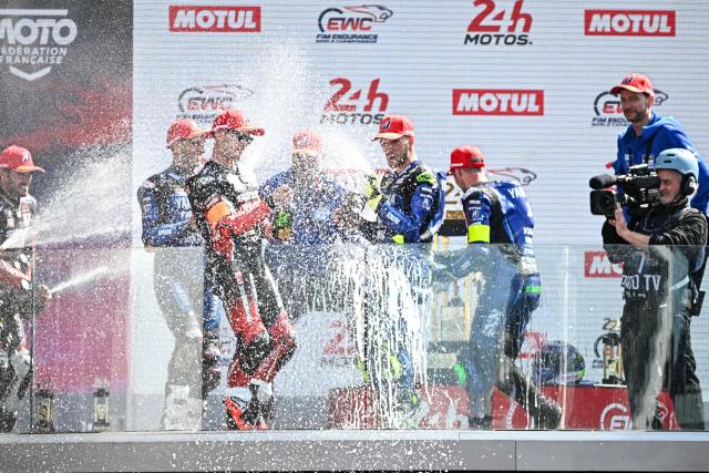 Winners Yart Yamaha Official formula EWC riders (R) and second-placed Yoshimura Sert Motul formula EWC riders (L) celebrate on the podium at the end of the 49th Le Mans 24-hours endurance moto race, in Le Mans, northwestern France, on April 19, 2026. (Photo by JULIEN DE ROSA / AFP)