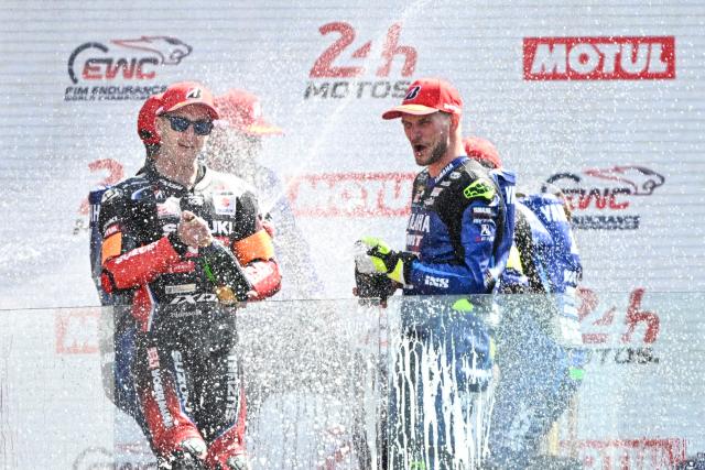 TOPSHOT - Winners Yart Yamaha Official formula EWC riders (R) and second-placed Yoshimura Sert Motul formula EWC riders (L) celebrate on the podium at the end of the 49th Le Mans 24-hours endurance moto race, in Le Mans, northwestern France, on April 19, 2026. (Photo by JULIEN DE ROSA / AFP)