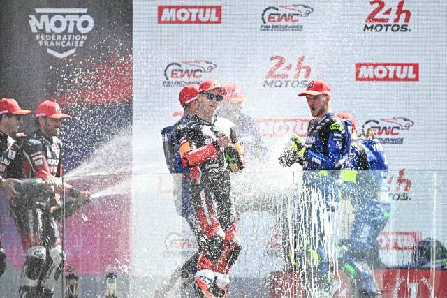 Winners Yart Yamaha Official formula EWC riders (R) and second-placed Yoshimura Sert Motul formula EWC riders (L) celebrate on the podium at the end of the 49th Le Mans 24-hours endurance moto race, in Le Mans, northwestern France, on April 19, 2026. (Photo by JULIEN DE ROSA / AFP)