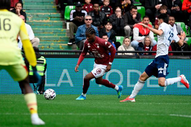 Metz’s Congolese forward #34 Nathan Mbala (C) runs with the ball in front of Paris FC's Belgian defender #28 Thibault De Smet (R) during the French L1 football match between FC Metz and Paris FC at the Stade Saint-Symphorien in Longeville-les-Metz, eastern France, on April 19, 2026. (Photo by Jean-Christophe VERHAEGEN / AFP)