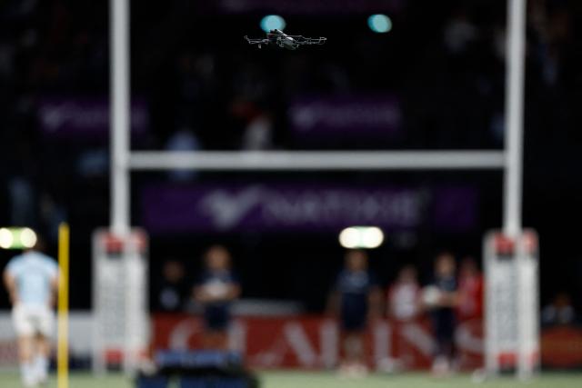 A tv broadcast drone flies over the pitch during teams warm up prior to the French Top14 rugby union match between Racing 92 and Stade Francais at the Paris La Defense Arena in Nanterre, on the outskirts of Paris, on April 19, 2026. (Photo by Kenzo TRIBOUILLARD / AFP)