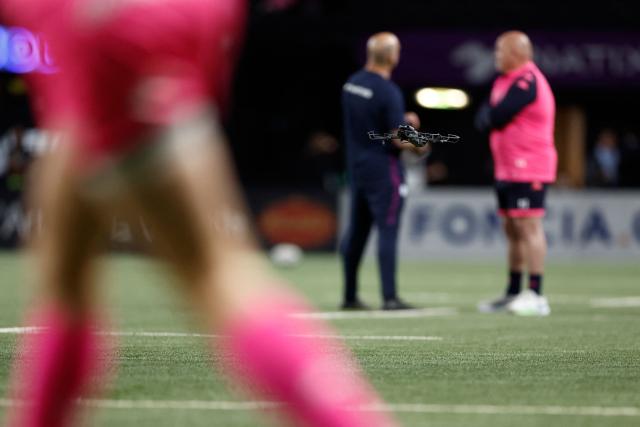 A tv broadcast drone flies over the pitch during teams warm up prior to the French Top14 rugby union match between Racing 92 and Stade Francais at the Paris La Defense Arena in Nanterre, on the outskirts of Paris, on April 19, 2026. (Photo by Kenzo TRIBOUILLARD / AFP)