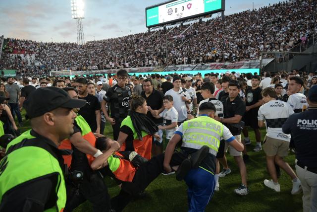 Fans of Cerro Porteno walk on the pitch after clashes with police officers during the Paraguayan tournament football match between Olimpia and Cerro Porteno at the Defensores del Chaco stadium in Asuncion on April 19, 2026. Several people were injured and at least a hundred were arrested following incidents that occurred during the Paraguayan football derby between Olimpia and Cerro Porteno, which was suspended in the first half in Asuncion on April 19, 2026. (Photo by Daniel DUARTE / AFP)