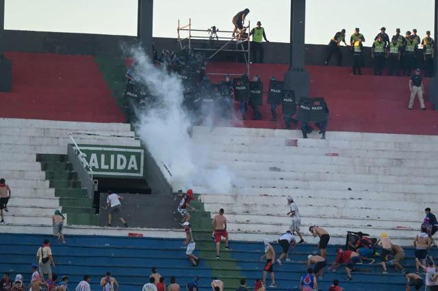 Fans of Cerro Porteno clash with police officers during the Paraguayan tournament football match between Olimpia and Cerro Porteno at the Defensores del Chaco stadium in Asuncion on April 19, 2026. Several people were injured and at least a hundred were arrested following incidents that occurred during the Paraguayan football derby between Olimpia and Cerro Porteno, which was suspended in the first half in Asuncion on April 19, 2026. (Photo by Pablo BURGOS / AFP)