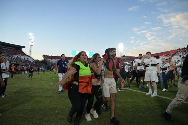 Fans of Cerro Porteno walk on the pitch after clashes with police officers during the Paraguayan tournament football match between Olimpia and Cerro Porteno at the Defensores del Chaco stadium in Asuncion on April 19, 2026. Several people were injured and at least a hundred were arrested following incidents that occurred during the Paraguayan football derby between Olimpia and Cerro Porteno, which was suspended in the first half in Asuncion on April 19, 2026. (Photo by Pablo BURGOS / AFP)