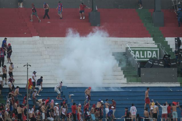 Fans of Cerro Porteno clash with police officers during the Paraguayan tournament football match between Olimpia and Cerro Porteno at the Defensores del Chaco stadium in Asuncion on April 19, 2026. Several people were injured and at least a hundred were arrested following incidents that occurred during the Paraguayan football derby between Olimpia and Cerro Porteno, which was suspended in the first half in Asuncion on April 19, 2026. (Photo by Daniel DUARTE / AFP)