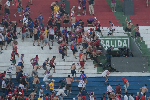Fans of Cerro Porteno clash with police officers during the Paraguayan tournament football match between Olimpia and Cerro Porteno at the Defensores del Chaco stadium in Asuncion on April 19, 2026. Several people were injured and at least a hundred were arrested following incidents that occurred during the Paraguayan football derby between Olimpia and Cerro Porteno, which was suspended in the first half in Asuncion on April 19, 2026. (Photo by Daniel DUARTE / AFP)