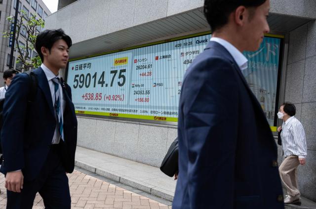 People walk past a display of the Nikkei Stock Average near the Tokyo Stock Exchange in Tokyo on April 20, 2026. (Photo by Andrew CABALLERO-REYNOLDS / AFP)