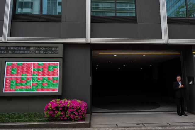 A man stands outside a parking garage next to a stocks display near the Tokyo Stock Exchange in Tokyo on April 20, 2026. (Photo by Andrew CABALLERO-REYNOLDS / AFP)