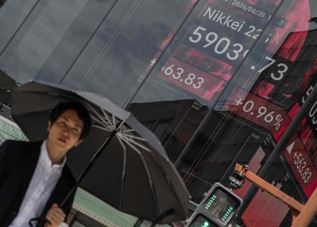 A man crosses the street near a board displaying the Nikkei Stock Average on the Tokyo Stock Exchange in Tokyo on April 20, 2026. (Photo by Andrew CABALLERO-REYNOLDS / AFP)