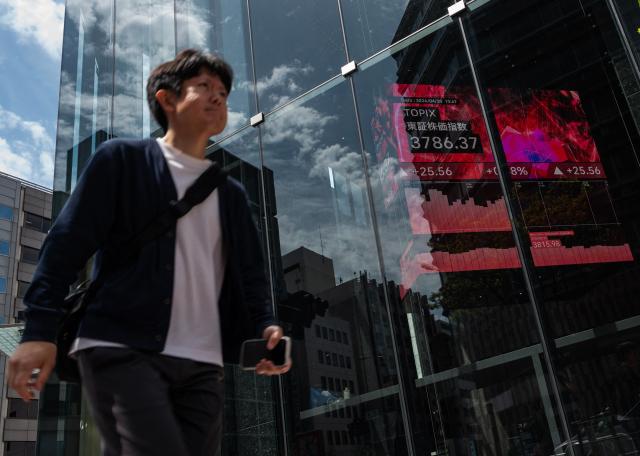 A man pass a building with a board displaying the Nikkei Stock Average on the Tokyo Stock Exchange in Tokyo on April 20, 2026. (Photo by Andrew CABALLERO-REYNOLDS / AFP)