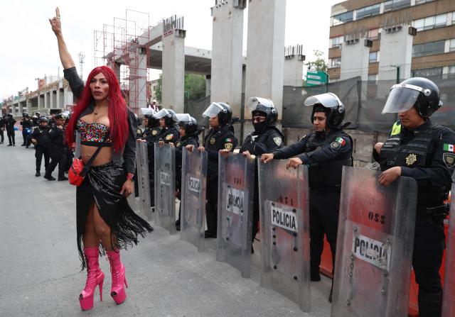 A transgender sex worker stands in front of Mexican riot police officers during a protest against the Gran Tenochtitlan bike path and the organisation of the World Cup in Mexico City on April 19, 2026. The Gran Tenochtitlan is an infrastructure project designed to connect Banorte Stadium (formerly Azteca Stadium) with other points of interest in Mexico City, according to the local government. (Photo by LUIS CORTES / AFP)
