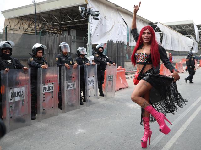 A transgender sex worker stands gestures in front of Mexican riot police officers during a protest against the Gran Tenochtitlan bike path and the organisation of the World Cup in Mexico City on April 19, 2026. The Gran Tenochtitlan is an infrastructure project designed to connect Banorte Stadium (formerly Azteca Stadium) with other points of interest in Mexico City, according to the local government. (Photo by LUIS CORTES / AFP)