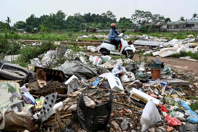 A woman rides an electric motorbike past a landfill in Hanoi on April 20, 2026. (Photo by Nhac NGUYEN / AFP)