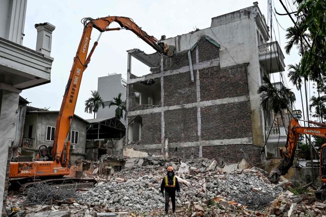 A worker stands next to an excavator at a building demolition site in Hanoi on April 20, 2026. (Photo by Nhac NGUYEN / AFP)