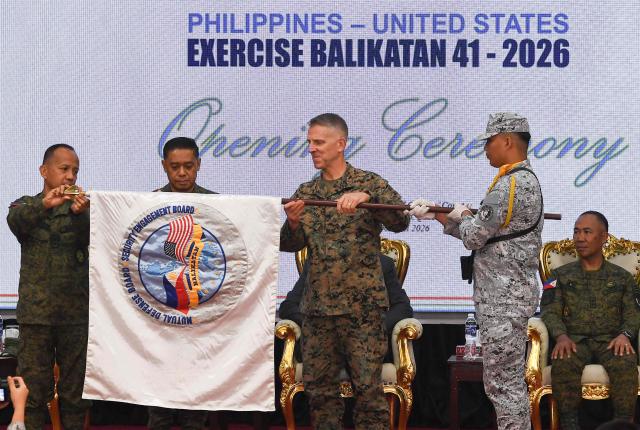 (L-R) Major General Francisco Lorenzo, Philippine exercise director, Philippine military Chief General Romeo Brawner, and US Lieutenant General Christian Wortman, Commanding General I Marine Expeditionary Force, unfurl the joint military exercise flag during the opening ceremony of the annual Balikatan (shoulder to shoulder) joint military exercise at Camp Aguinaldo in Quezon city, suburban Manila on Aril 20, 2026. Thousands of American and Philippine troops, joined for the first time by a significant contingent of Japanese forces, began annual military exercises on April 20 set against the backdrop of the Middle East war. (Photo by Ted ALJIBE / AFP)