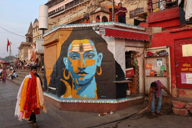 A vendor sweeps the floor as he opens his shop next to a mural of Hindu deity Shiva at Ahilyabai Ghat along the banks of the river Ganges in Varanasi on April 20, 2026. (Photo by Niharika KULKARNI / AFP)