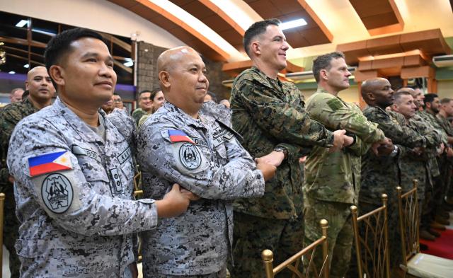 Philippine military (L) officers join hands with US marines officers during the opening ceremony of the annual Balikatan (shoulder to shoulder) joint military exercise at Camp Aguinaldo in Quezon city, suburban Manila on April 20, 2026. Thousands of American and Philippine troops, joined for the first time by a significant contingent of Japanese forces, began annual military exercises on April 20 set against the backdrop of the Middle East war. (Photo by Ted ALJIBE / AFP)
