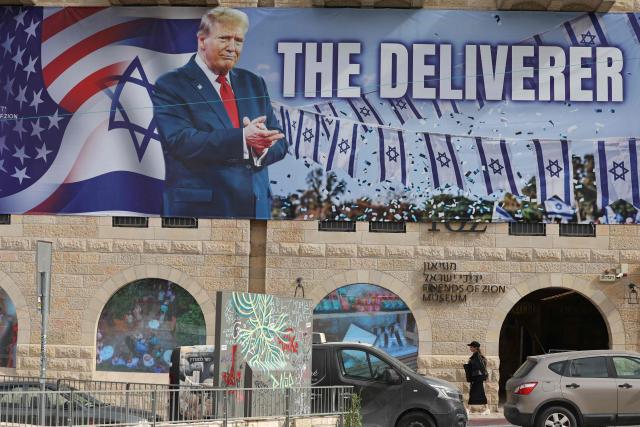 A woman walks past a banner depicting US President Donald Trump with the slogan “The Deliverer” in Jerusalem on April 20, 2026. Iran is not currently planning to attend talks with the United States, state media said, after the US president ordered US negotiators to travel to Pakistan on April 20, just days before a ceasefire in the Middle East expires. (Photo by AHMAD GHARABLI / AFP) / 
