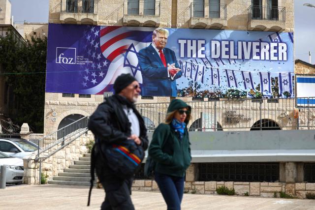 People walk past a banner depicting US President Donald Trump with the slogan “The Deliverer” in Jerusalem on April 20, 2026. Iran is not currently planning to attend talks with the United States, state media said, after the US president ordered US negotiators to travel to Pakistan on April 20, just days before a ceasefire in the Middle East expires. (Photo by AHMAD GHARABLI / AFP) / 