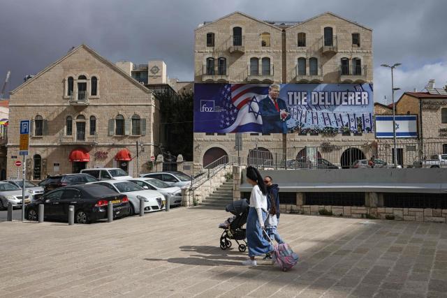 People walk past a banner depicting US President Donald Trump with the slogan “The Deliverer” in Jerusalem on April 20, 2026. Iran is not currently planning to attend talks with the United States, state media said, after the US president ordered US negotiators to travel to Pakistan on April 20, just days before a ceasefire in the Middle East expires. (Photo by AHMAD GHARABLI / AFP) / 