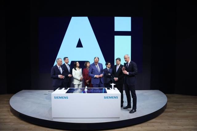 President and CEO of Siemens AG Roland Busch (R) speaks as German Chancellor Friedrich Merz (C) listens during a tour of the Hannover industrial trade fair for mechanical and electrical engineering and digital industries, in Hannover, northern Germany on April 20, 2026. The fair opens its doors to the public on April 20 and will be running until April 24, 2026. (Photo by Ronny HARTMANN / AFP)