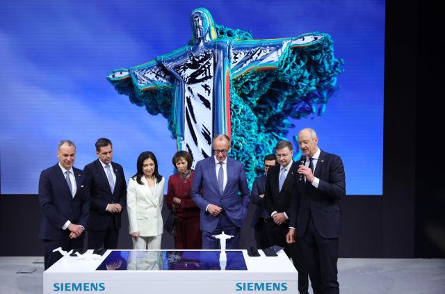 German Chancellor Friedrich Merz (C-R), his wife Charlotte Merz, German Economy and Energy Minister Katherina Reiche (3rd L) and Lower Saxony's State Premier Olaf Lies (2nd L) listen to Siemens CEO Roland Busch (R) during a tour of the Hannover Messer industrial trade fair for mechanical and electrical engineering and digital industries, in Hanover, northern Germany on April 20, 2026. The fair opens its doors to the public on April 20 and will be running until April 24, 2026. (Photo by Ronny HARTMANN / AFP)