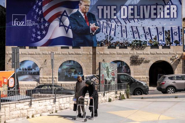 People walk past a banner depicting US President Donald Trump with the slogan “The Deliverer” in Jerusalem on April 20, 2026. Iran is not currently planning to attend talks with the United States, state media said, after the US president ordered US negotiators to travel to Pakistan on April 20, just days before a ceasefire in the Middle East expires. (Photo by JOHN WESSELS / AFP) / 