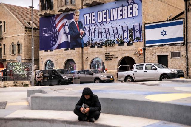 A man sits in front of a banner depicting US President Donald Trump with the slogan “The Deliverer” in Jerusalem on April 20, 2026. Iran is not currently planning to attend talks with the United States, state media said, after the US president ordered US negotiators to travel to Pakistan on April 20, just days before a ceasefire in the Middle East expires. (Photo by JOHN WESSELS / AFP) / 