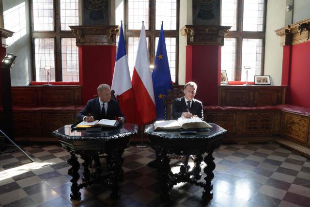 French President Emmanuel Macron (R) and Poland's Prime Minister Donald Tusk sign the golden book at the Main Town Hall in Gdansk, Poland, on April 20, 2026 during the French President's one-day-visit to Poland. (Photo by Ludovic MARIN / AFP)